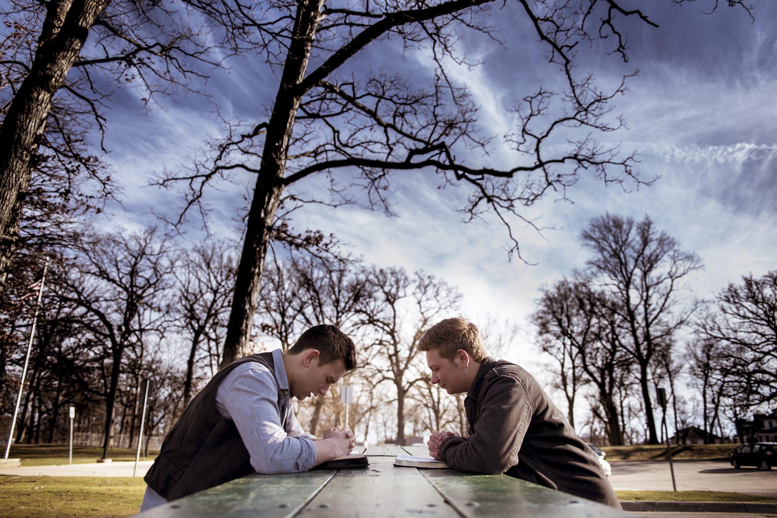 Men sitting on a bench with bibles and praying in a garden under sunlight with a blurry background